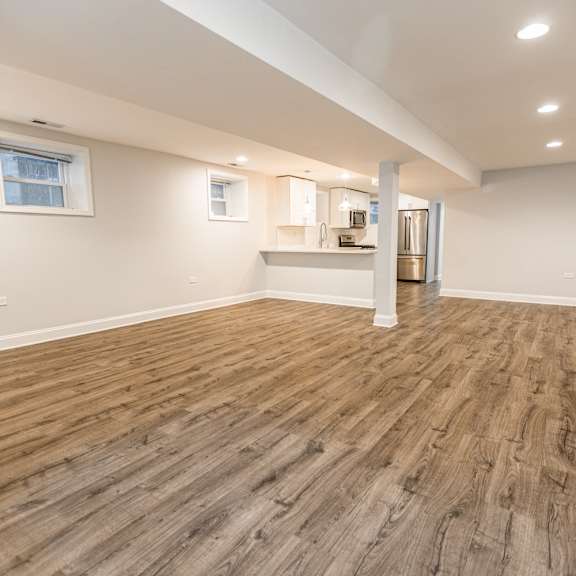 a room with wooden flooring and a kitchenette in the background.