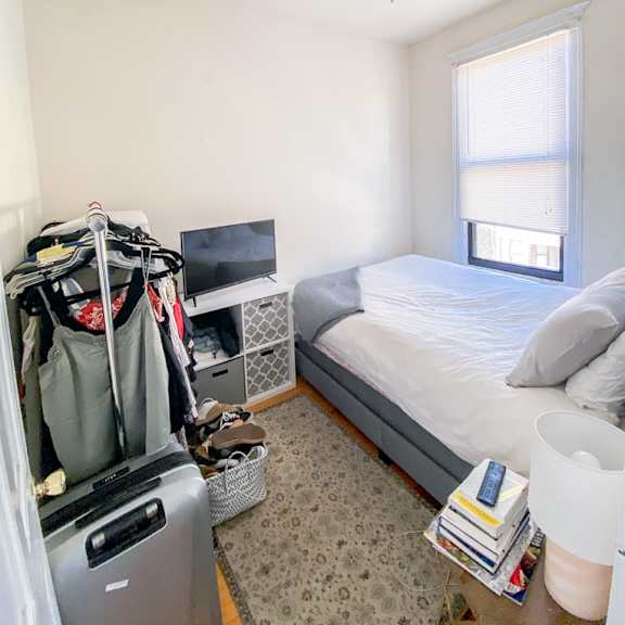 a bedroom with a bed, a fan, a window, and a clothing rack.