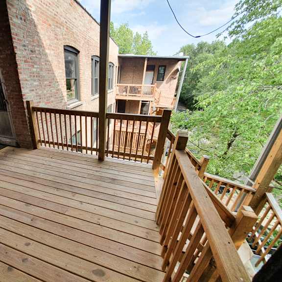 a wooden deck with a railing and a brick building in the background.