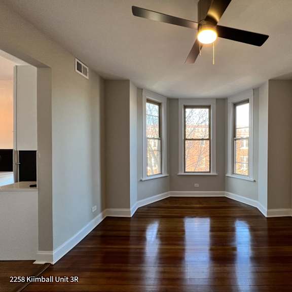 a room with a ceiling fan and three windows.