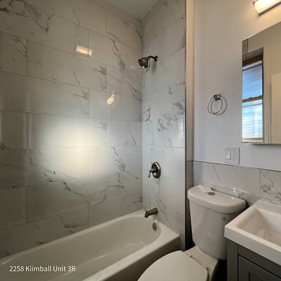 a white bathroom with a marble tile wall and a tub, toilet, and sink.