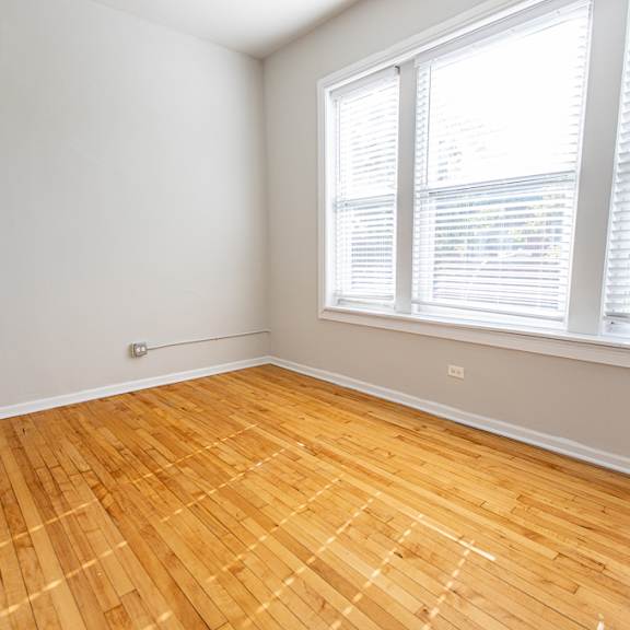 a room with wooden flooring and a window with blinds.