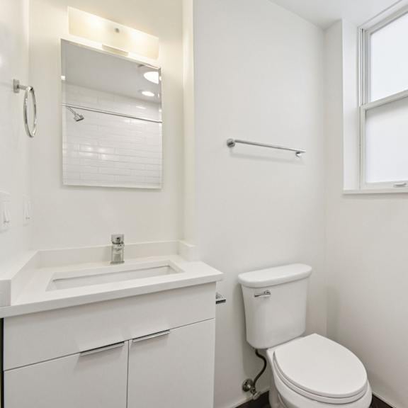 a white bathroom with a toilet, sink, and mirror.