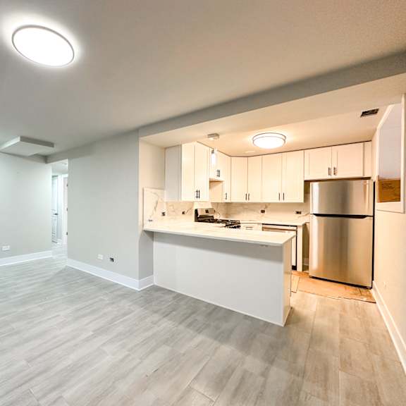 an empty living room with a kitchen with stainless steel appliances