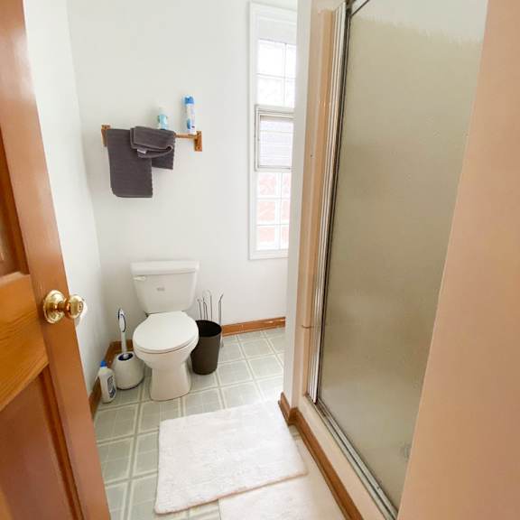 a bathroom with a toilet, a trash can, a towel rack, and a rug.