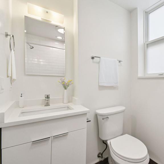 a white bathroom with a toilet, sink, and mirror.