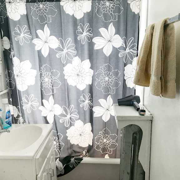 a bathroom with a white sink, a towel hanging on the wall, and a shower curtain with a floral pattern.