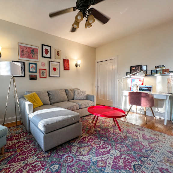 a living room with a grey couch, a red table, and a striped ottoman.