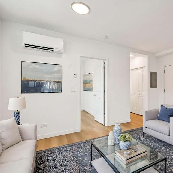 a living room with a white couch, two grey armchairs, a glass coffee table, and a painting on the wall.