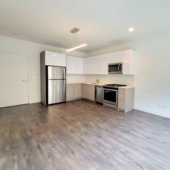 an empty living room with a kitchen with stainless steel appliances