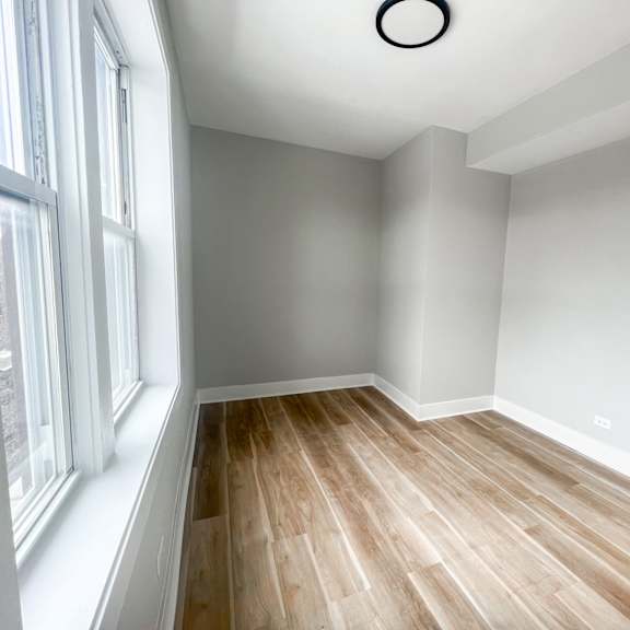 a room with a window on the left and a wooden floor.