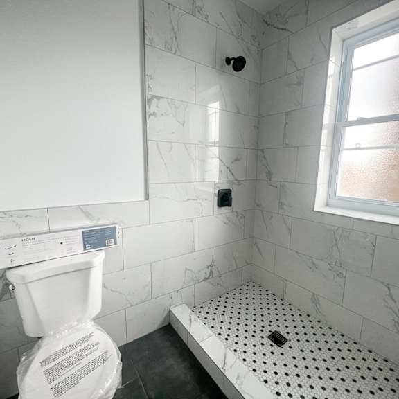 a white toilet in a bathroom with a marble wall and a window.