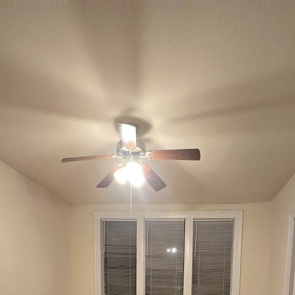 a ceiling fan with lights is on in a room with wood paneling.