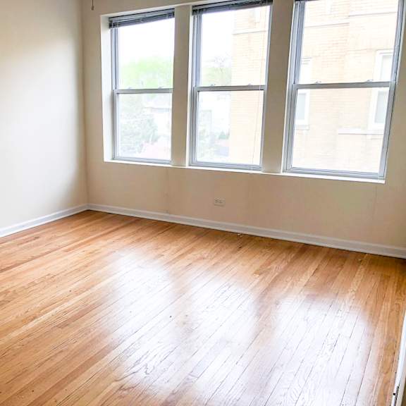 an empty room with wooden floors and three windows