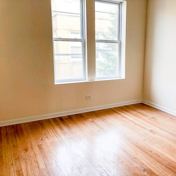 an empty room with wooden floors and two windows