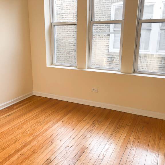 an empty room with wooden floors and three windows