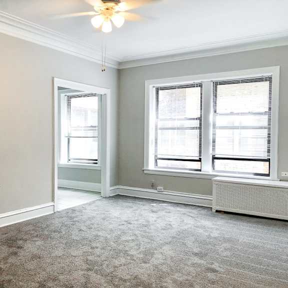 an empty living room with two windows and a ceiling fan