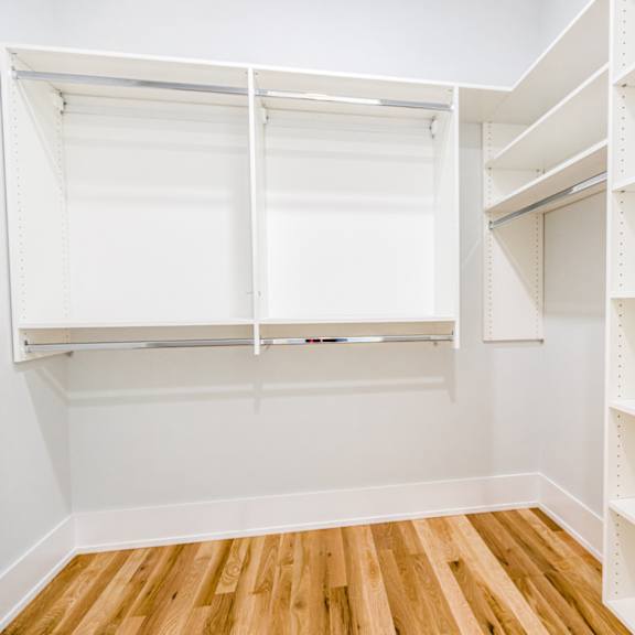 an empty closet with white shelves and a wood floor