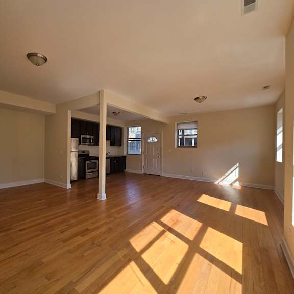 an empty living room with wood floors and a kitchen