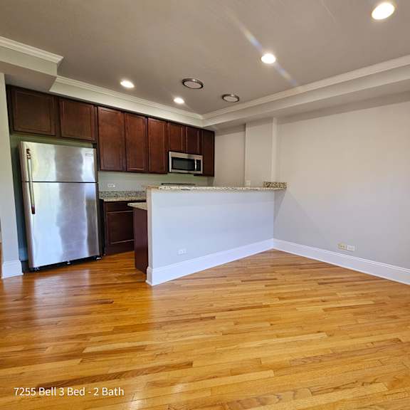 an empty living room and kitchen with wood flooring and a refrigerator