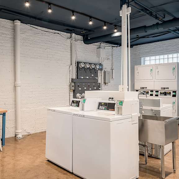 a white industrial machine sits in a room with a white brick wall and a painting of a desert scene hanging on the wall.