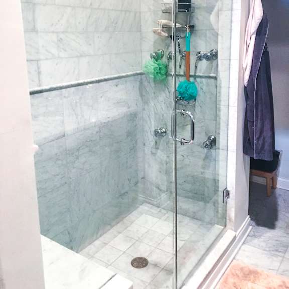 a shower with a glass door and a marble wall.
