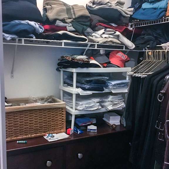 a messy room with clothes on shelves and a basket on a dresser.