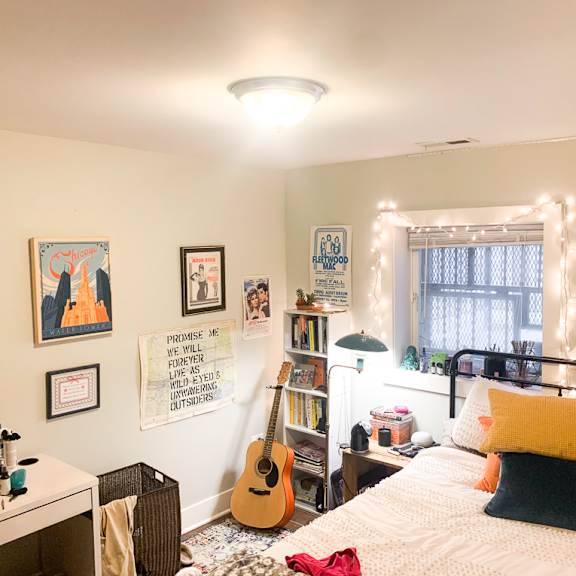 a bedroom with a bed, a desk, a guitar, and a window with lights.