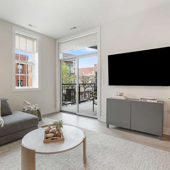 a living room with a grey couch, a white coffee table, and a black tv mounted on the wall.