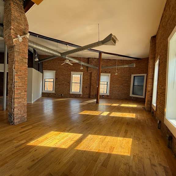 a large empty room with wooden floors and exposed pipes and brick pillars.