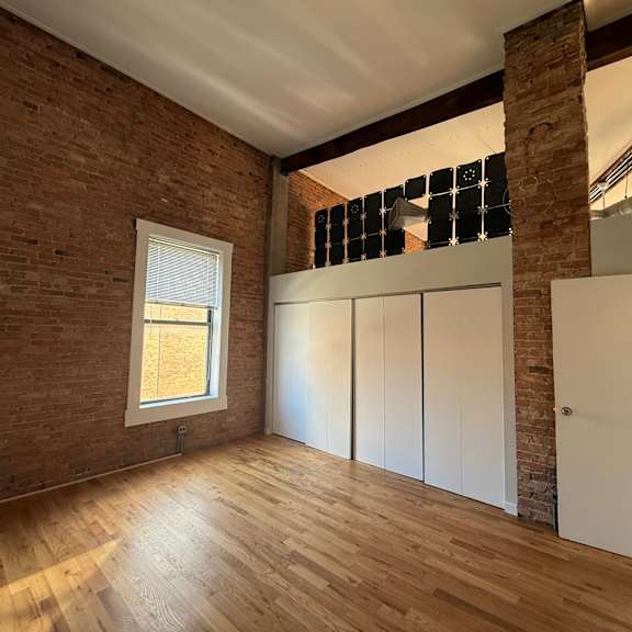 a room with wooden floors and a brick wall with a window.