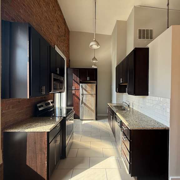 a kitchen with dark brown cabinets and a brick wall.