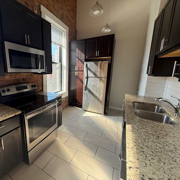 a kitchen with black cabinets and a brick wall.