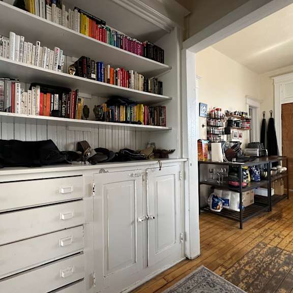 a room with a bookshelf filled with books and a white cabinet with drawers.