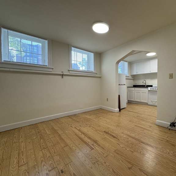 a room with wooden floors and a kitchen area in the background.