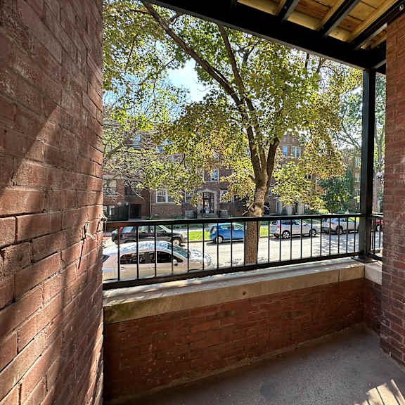 a balcony with a brick wall and a metal railing overlooking a parking lot.