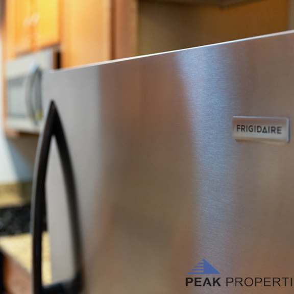a stainless steel refrigerator with a frigidaire logo and a peak properties logo.
