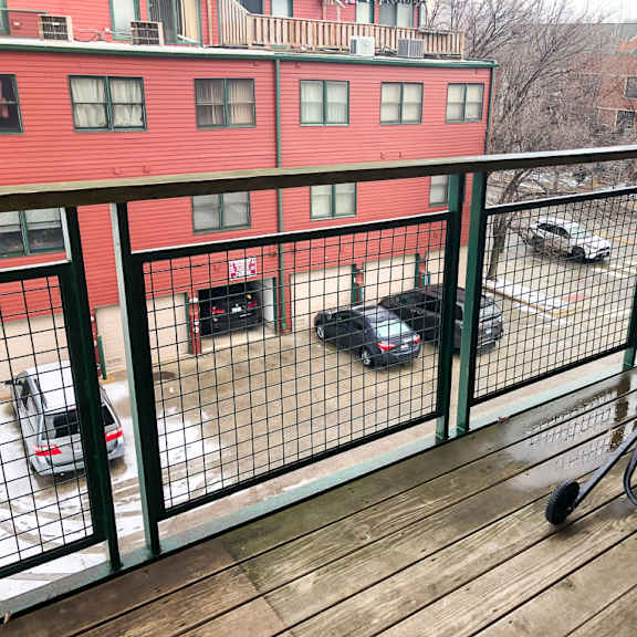 a balcony with a black grill and cars parked in the background.