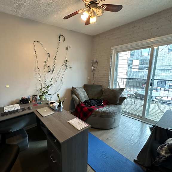 a room with a desk, a couch, a chair, and a ceiling fan.