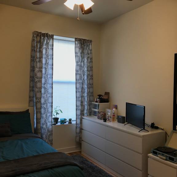 a bedroom with a bed, dresser, and window with curtains.
