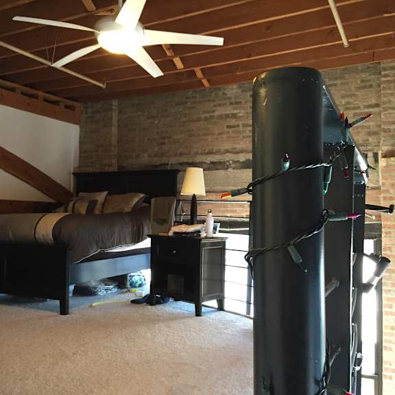 a room with a bed, a ceiling fan, and a brick wall.