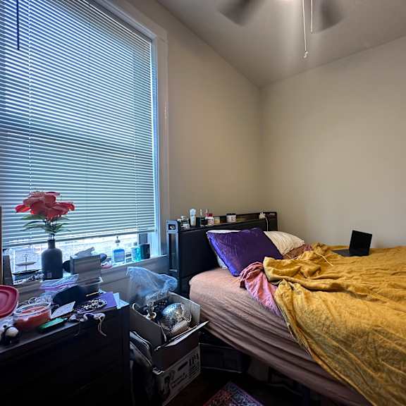 a bedroom with a bed, nightstand, and window with blinds.