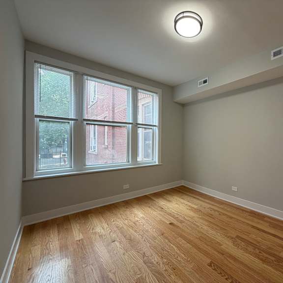 a room with wooden floors and a window showing a view of a red building outside.