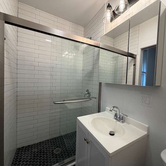 a modern bathroom with a glass shower enclosure and a white tiled wall.