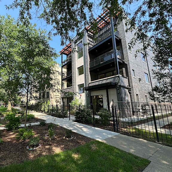 a modern building with a balcony is surrounded by trees and a black fence.