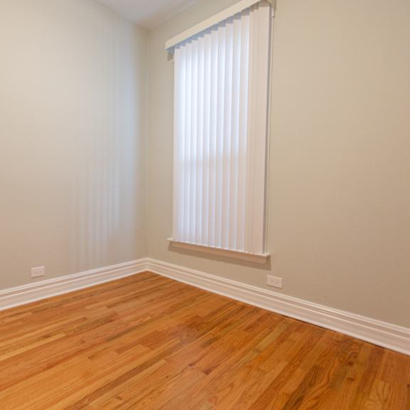 a room with wooden flooring and a window with blinds.