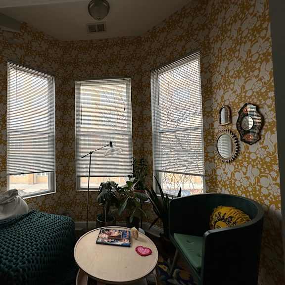 a room with a patterned wallpaper and two windows with blinds.