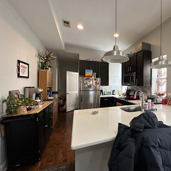 a kitchen with a white counter top and a person in a black jacket sitting at the counter.