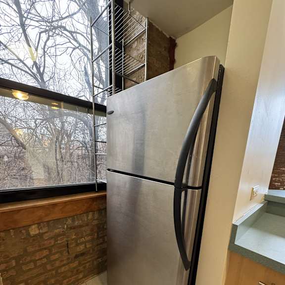 a stainless steel refrigerator in a kitchen with a brick wall and a window.