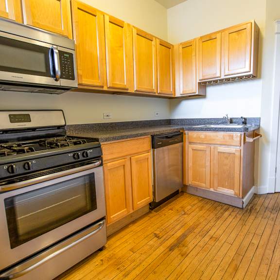 a kitchen with wood flooring and stainless steel appliances and wooden cabinets